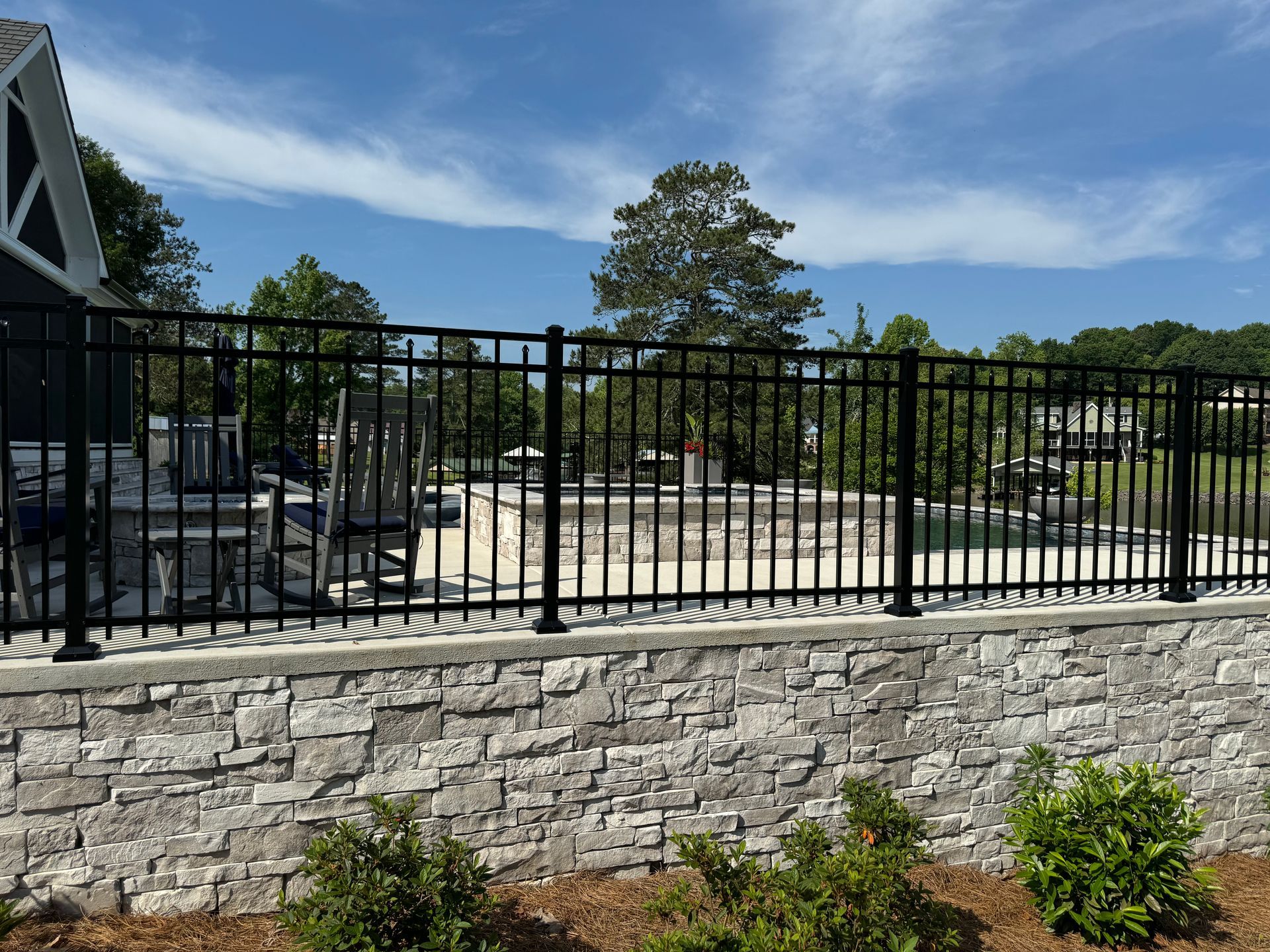 A fence surrounds a stone wall with a pool in the background