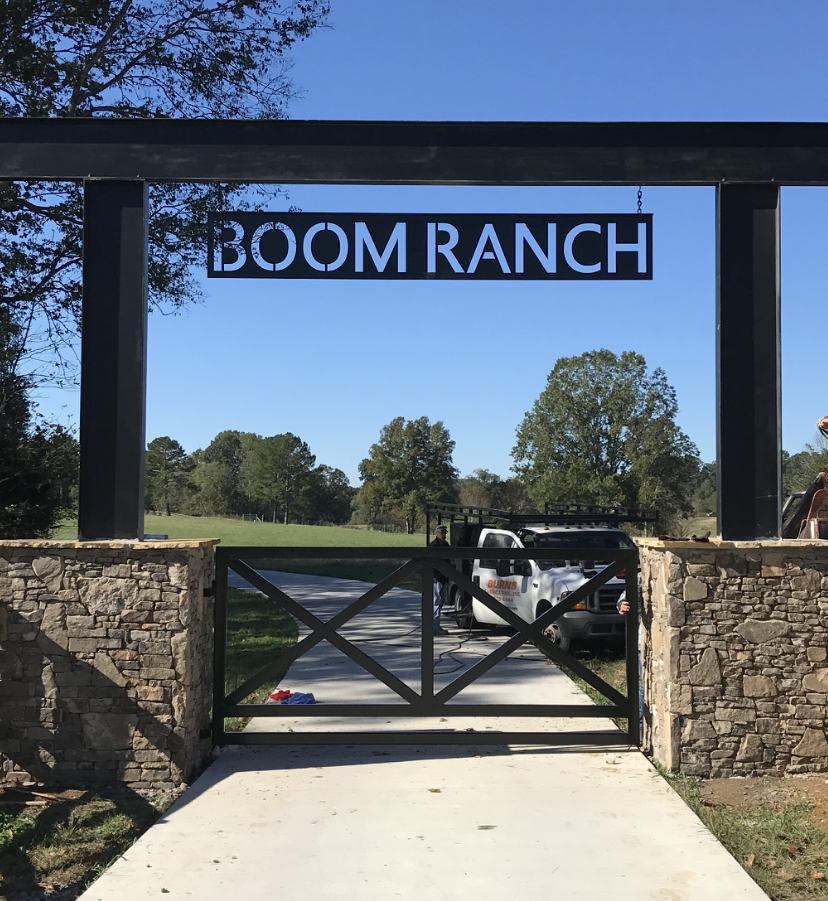 A sign for boom ranch hangs over a gate