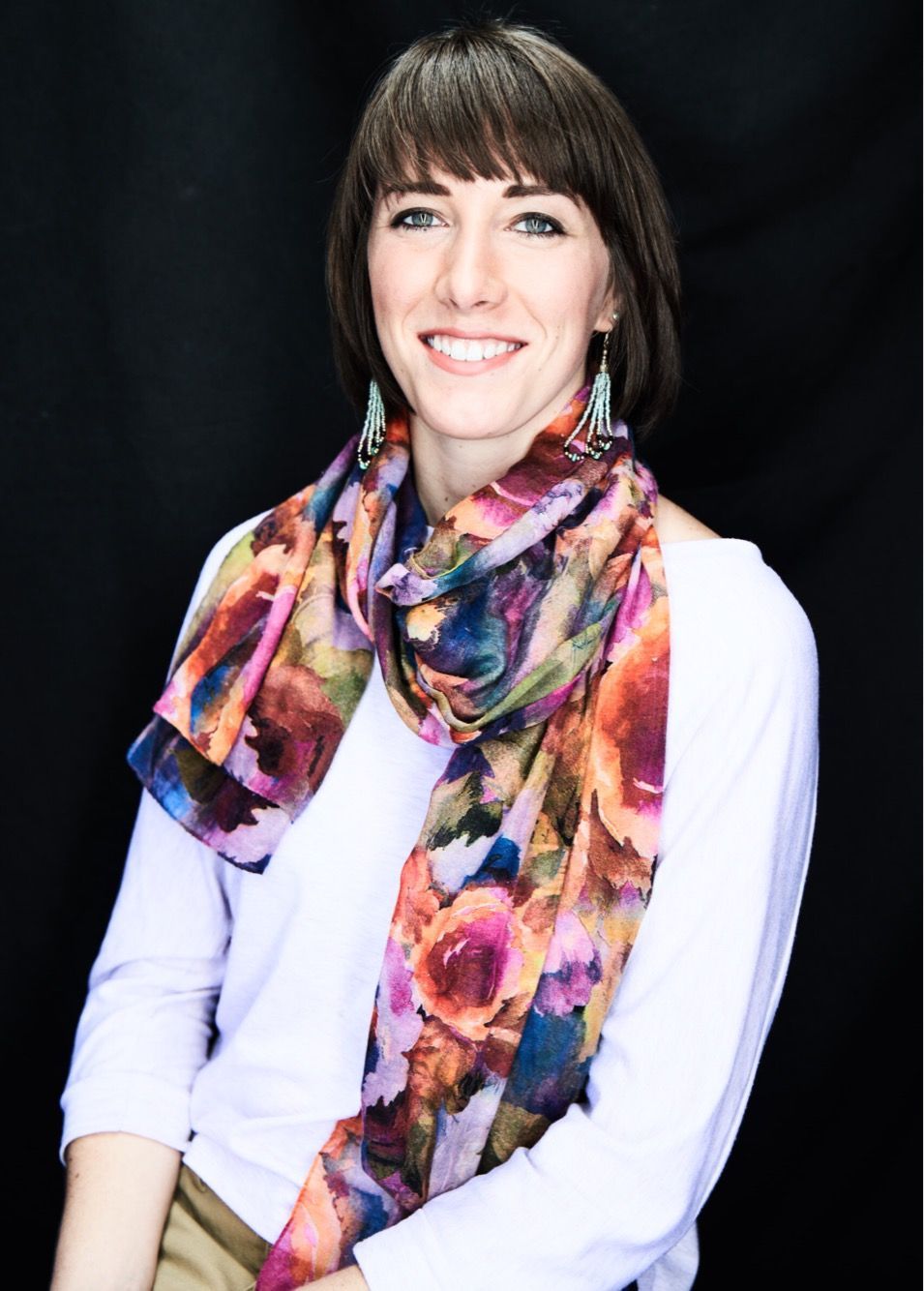 A woman wearing a floral scarf and earrings smiles for the camera