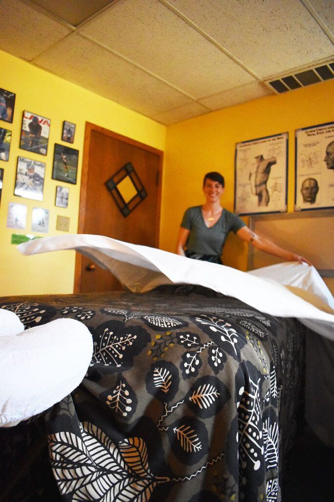 A woman is making a bed in a room with pictures on the wall