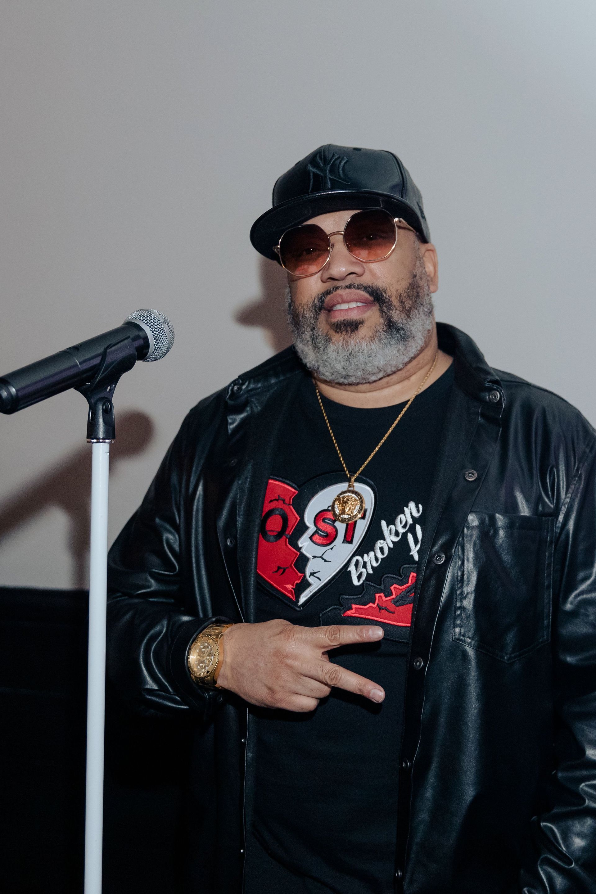 A man with a beard and sunglasses is standing in front of a microphone.