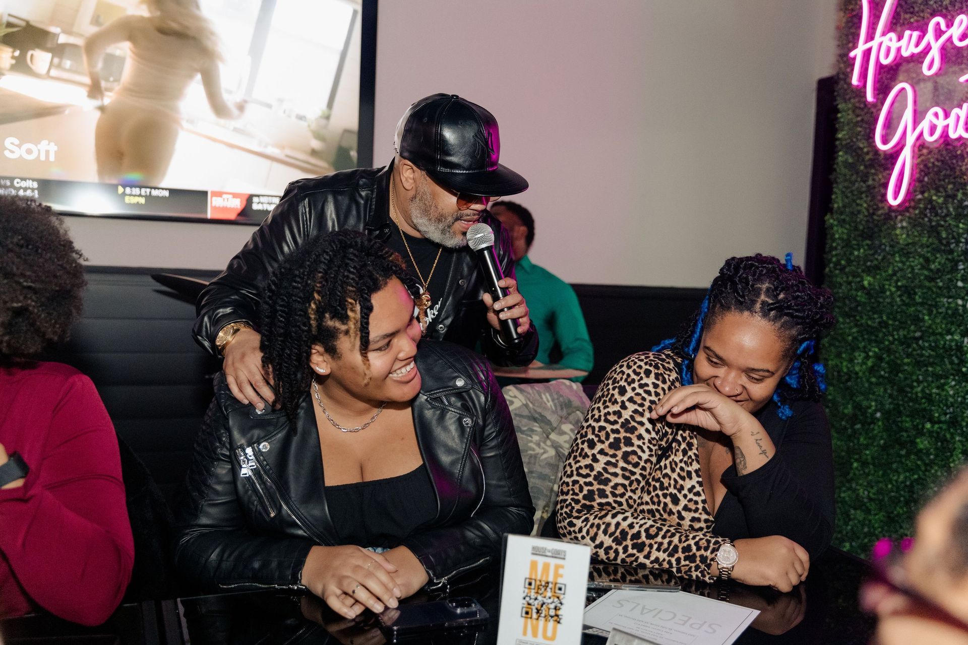 A man is holding a microphone while sitting at a table with two women.