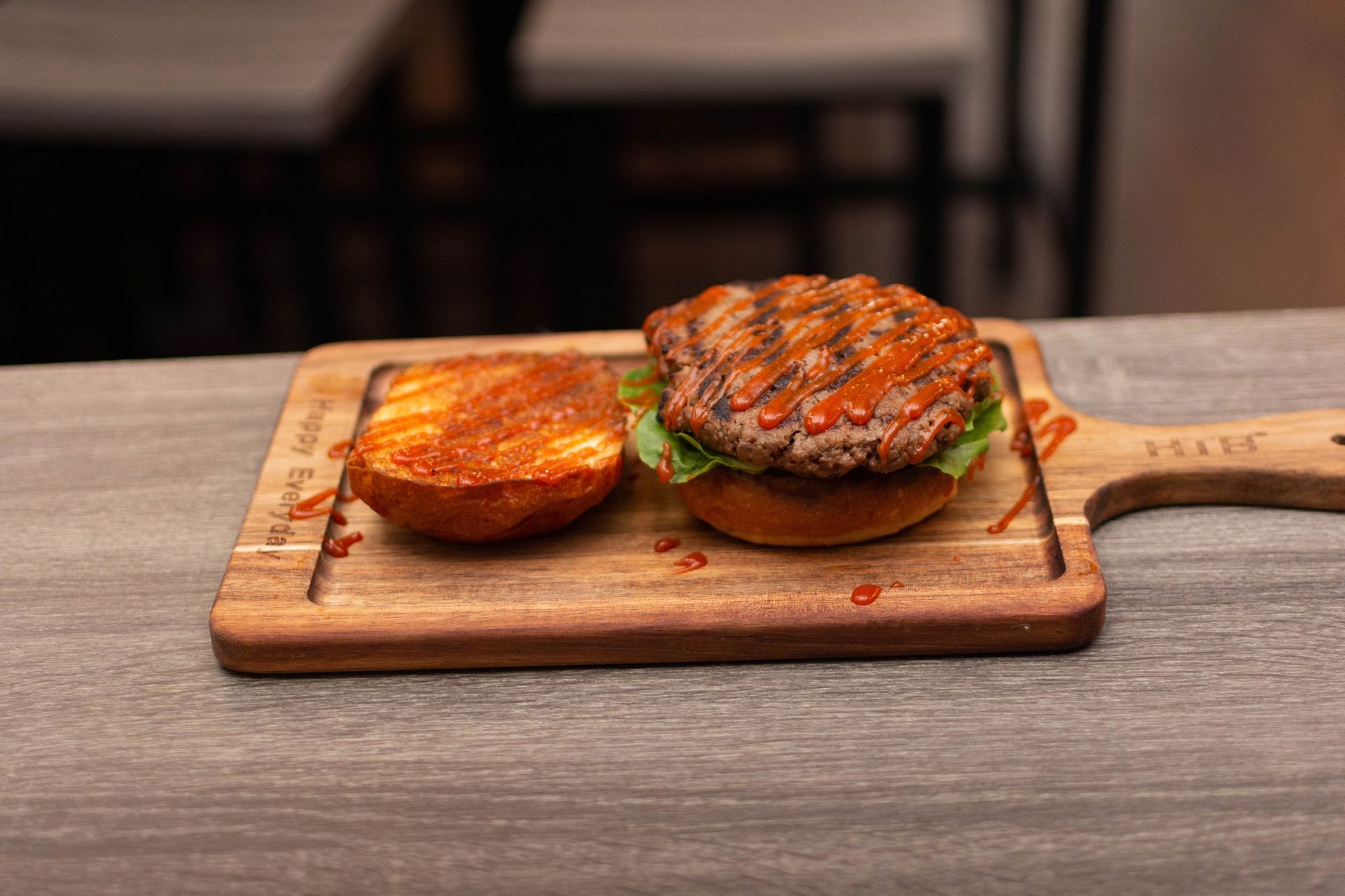 A hamburger is sitting on a wooden cutting board on a table.