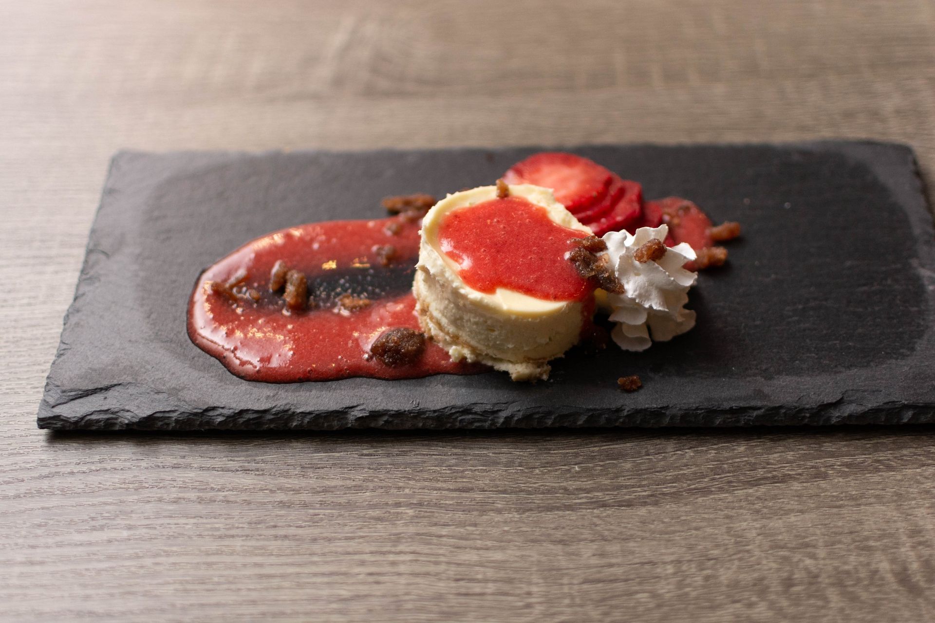A cheesecake with strawberries and whipped cream on a black plate.