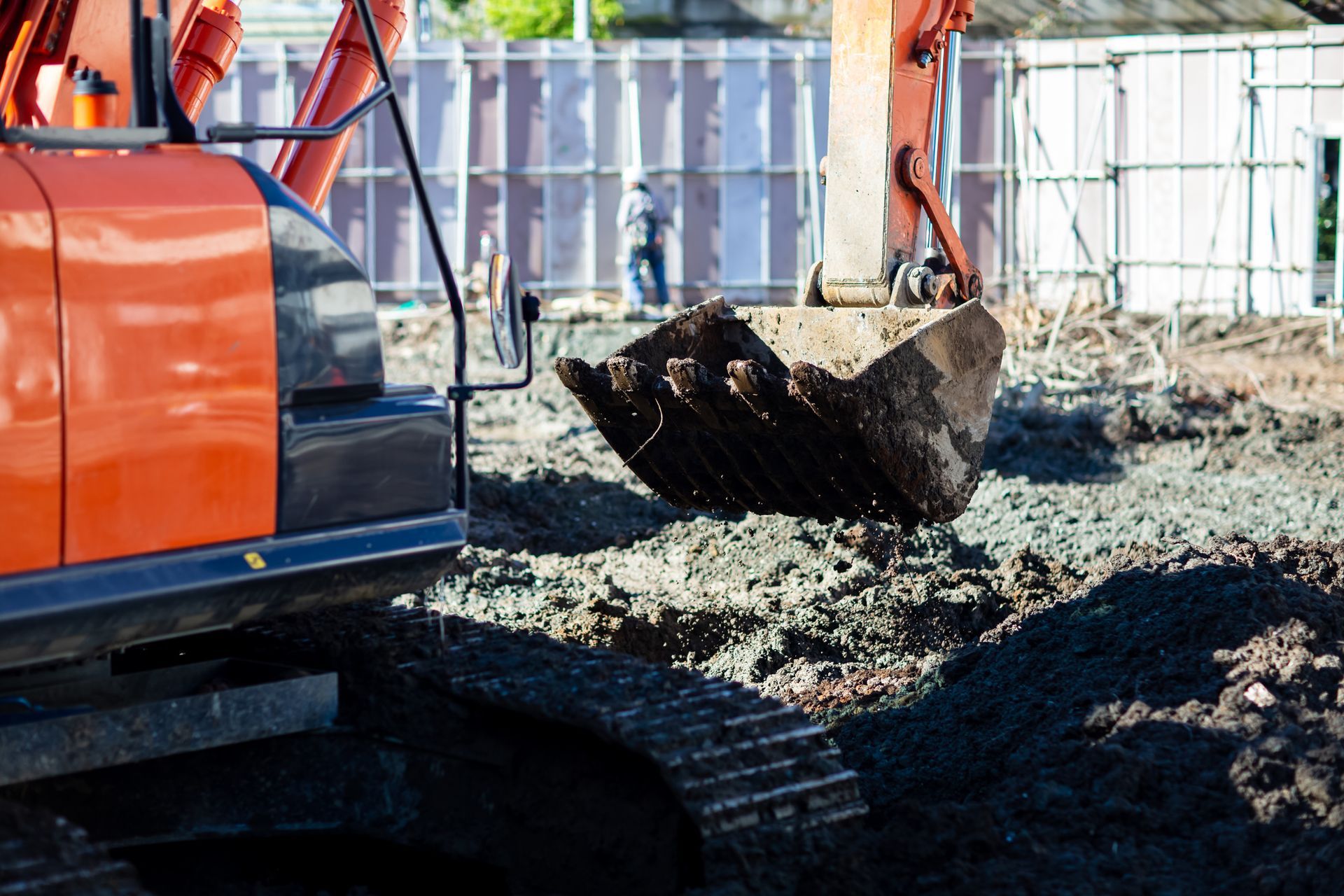 A large orange excavator is digging a hole in a dirt field.