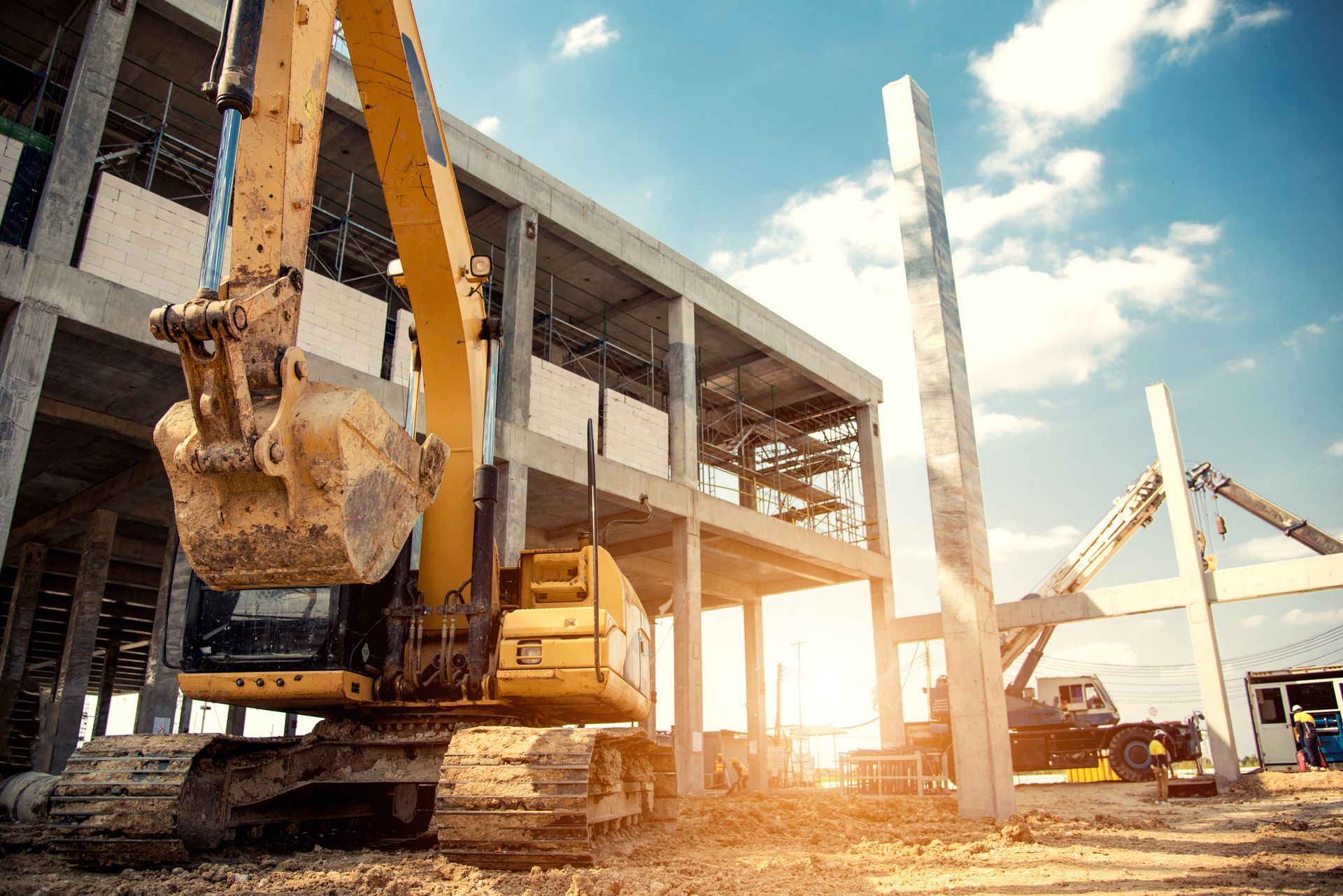A yellow excavator is sitting in front of a building under construction.