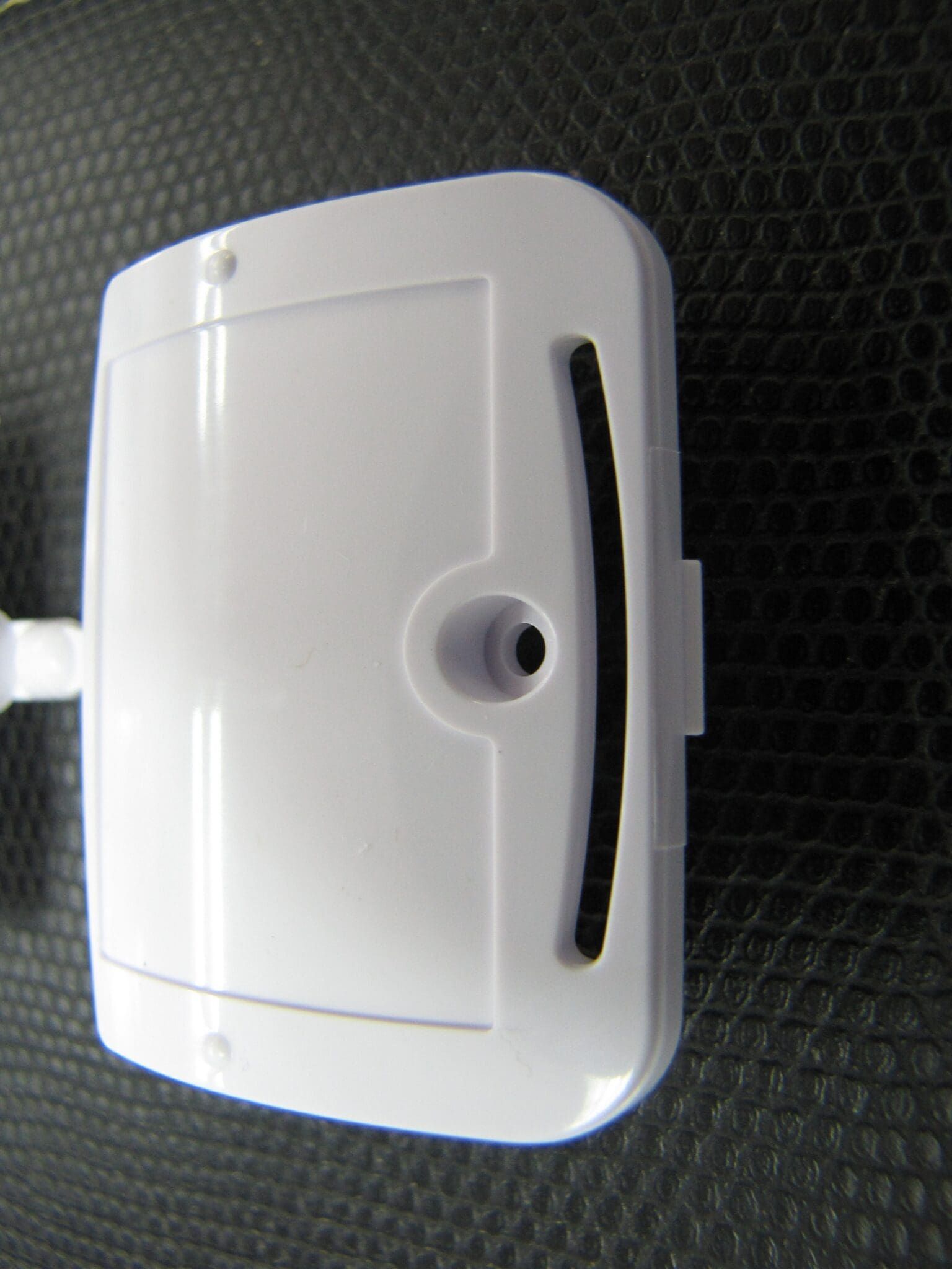 White plastic object with curved slot and nozzle, on a textured black surface.