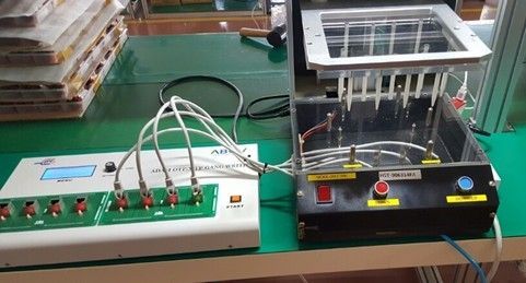 Electronics lab setup with control panel, wires, and a clear chamber apparatus on a workbench