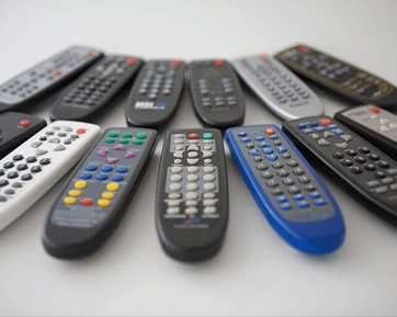 Assortment of various TV remote controls arranged in a radial pattern on a white surface.