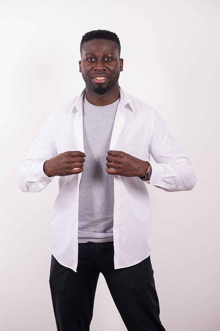 A man wearing a white shirt and black pants is standing in front of a white wall.