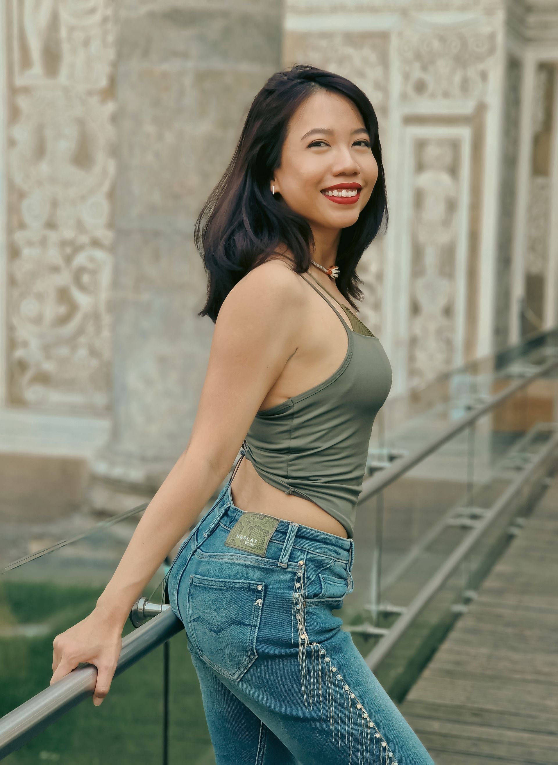 A woman in a green tank top and jeans is leaning on a railing.