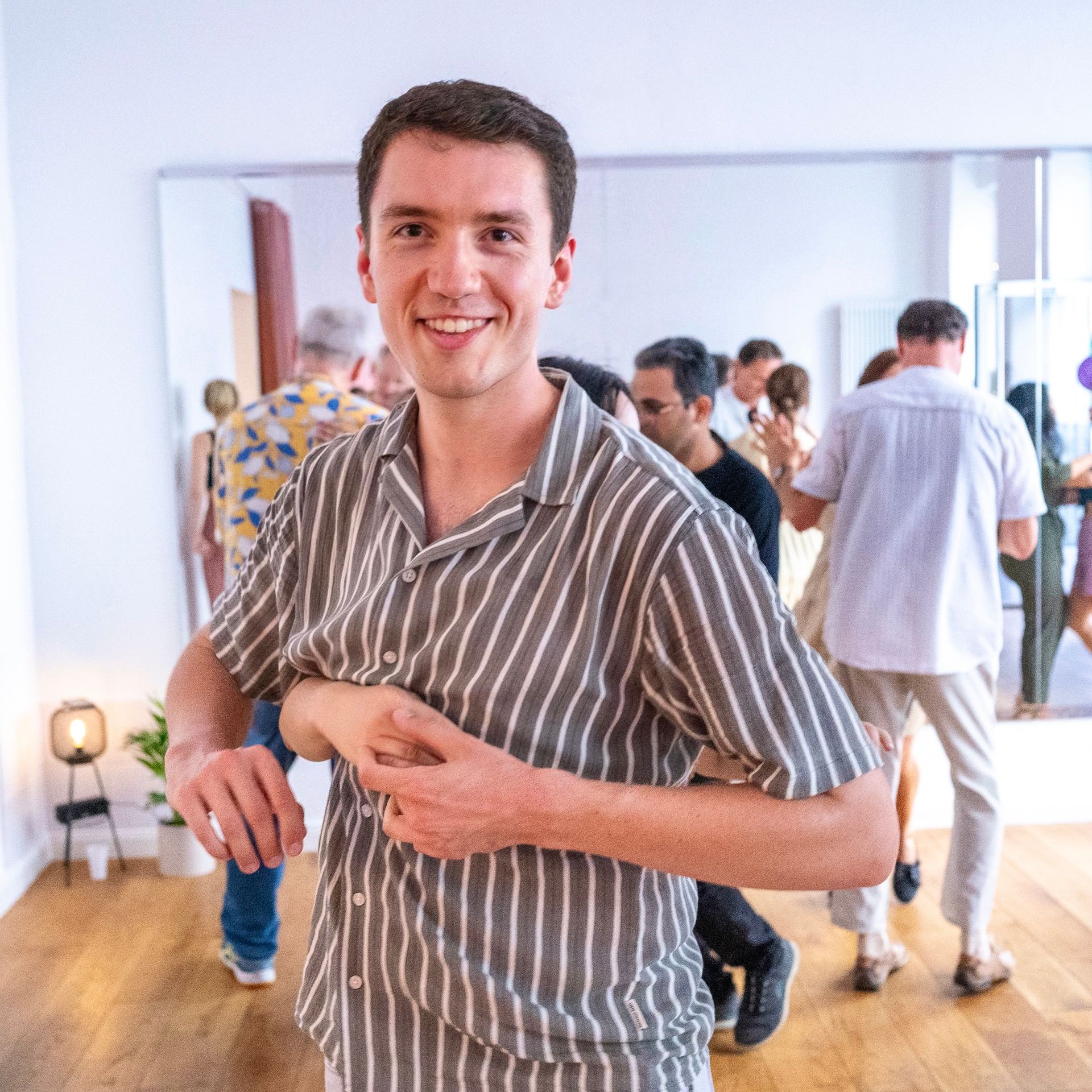 A man in a striped shirt is dancing in a room with other people.