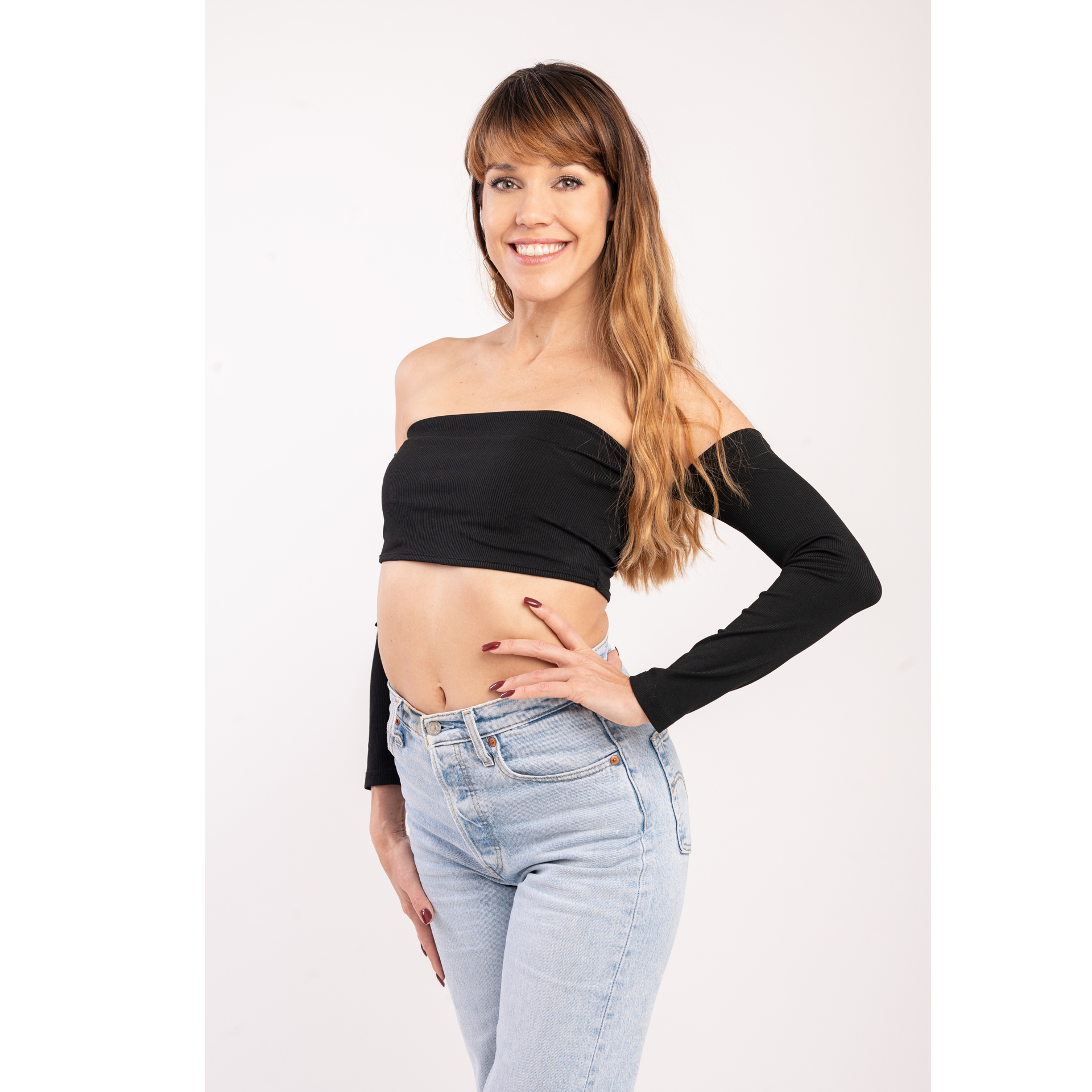 A woman in a white crop top and blue pants is standing with her hands on her hips.