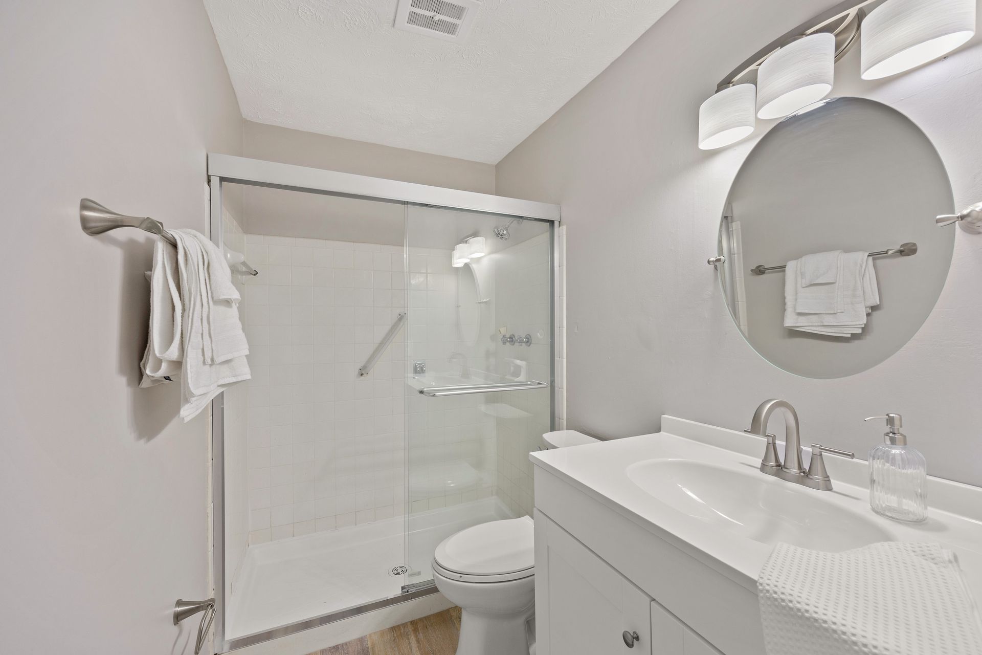 Modern apartment bathroom with glass-enclosed shower, vanity, and large mirror.