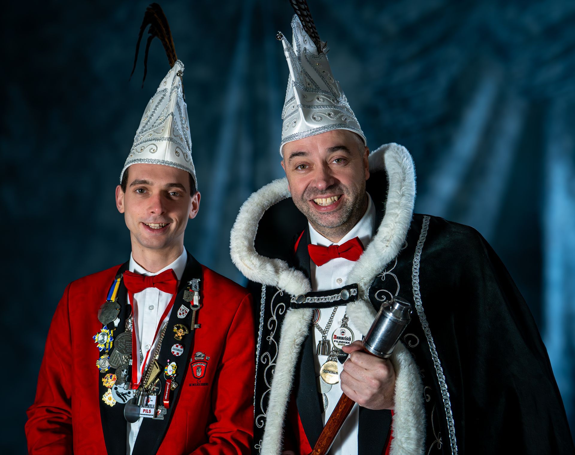 Twee mannen in kostuums poseren voor een foto en een van hen steekt zijn duim omhoog.
