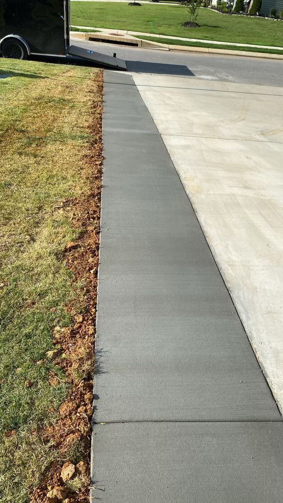 A sidewalk next to a driveway with a trailer parked on the side of the road.