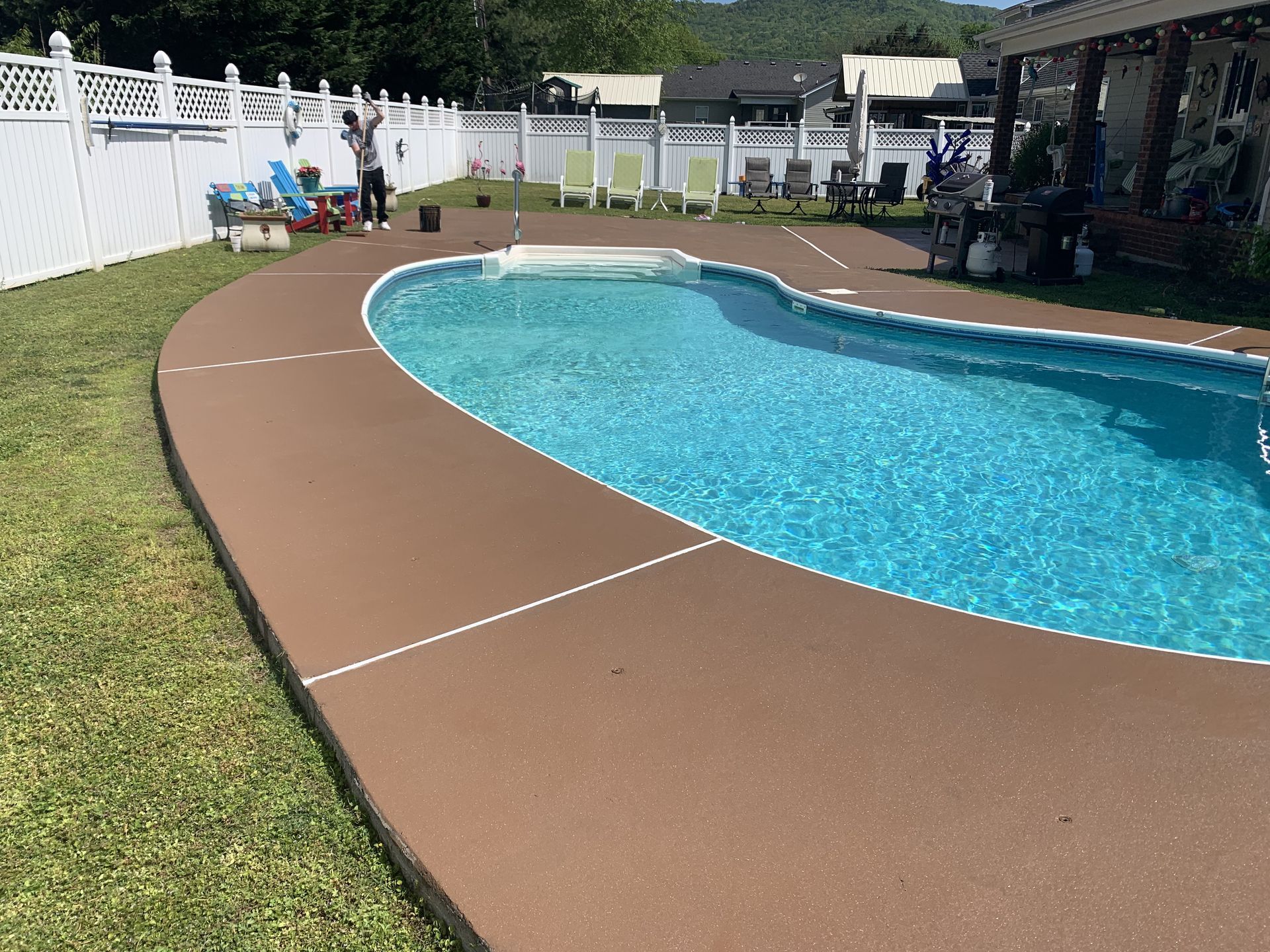 A large swimming pool in a backyard with a brown concrete deck.