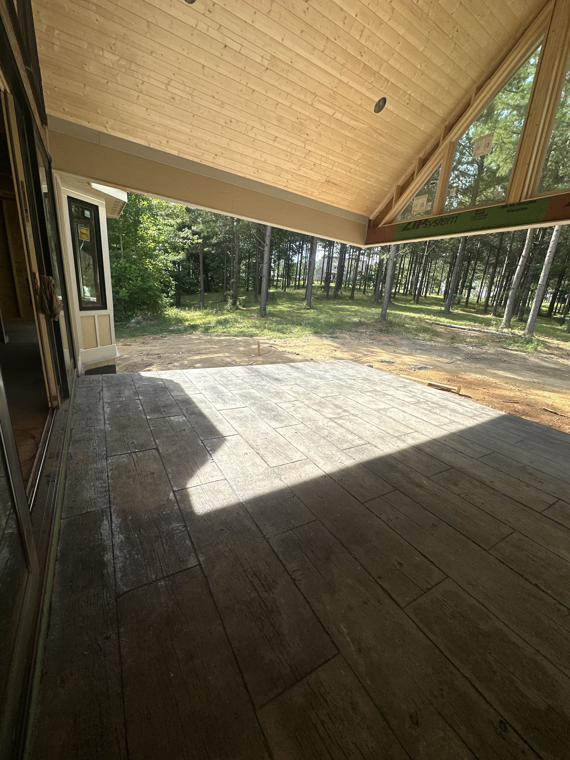 A large covered porch with a lot of windows and trees in the background.