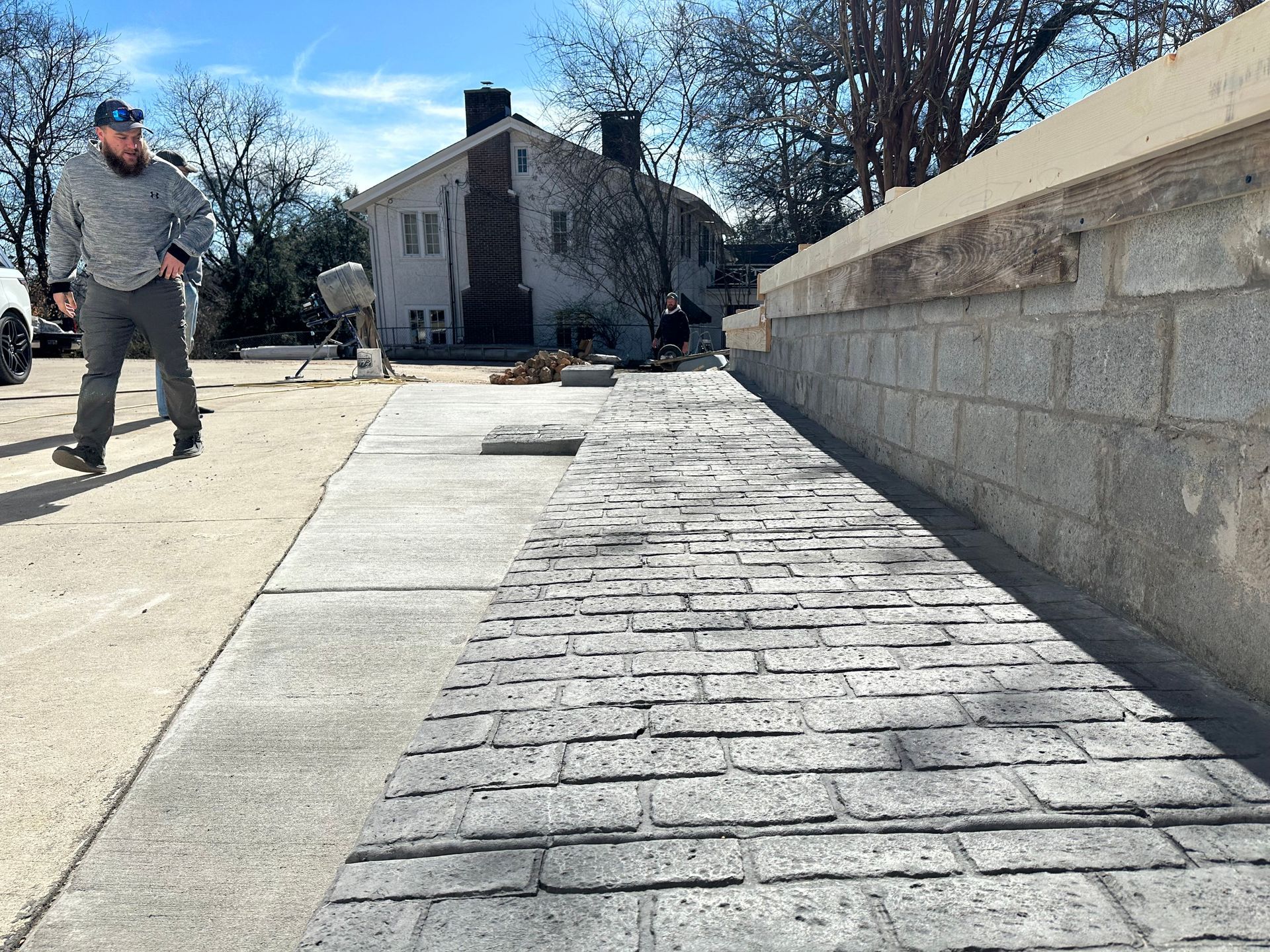 A man is walking down a sidewalk next to a brick wall.