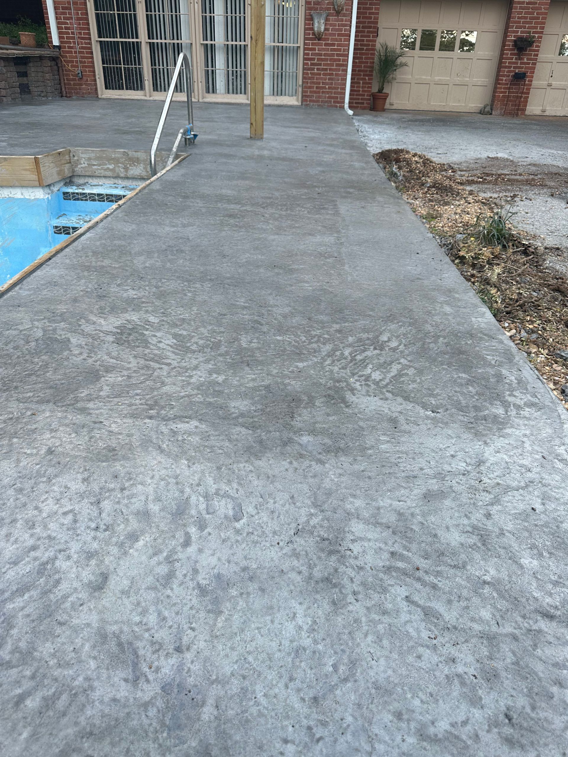 A concrete walkway leading to a swimming pool next to a house.