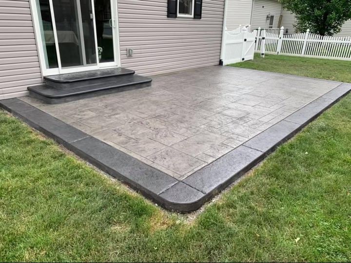 A concrete patio with steps and a fence in front of a house.