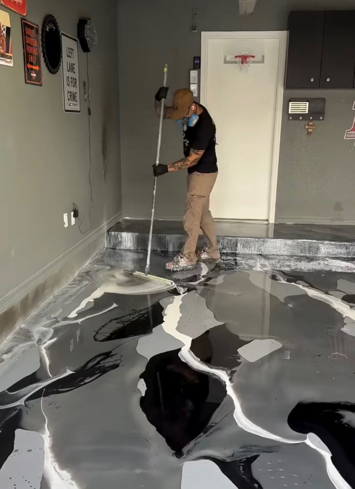 A man is painting a black and white floor in a garage.