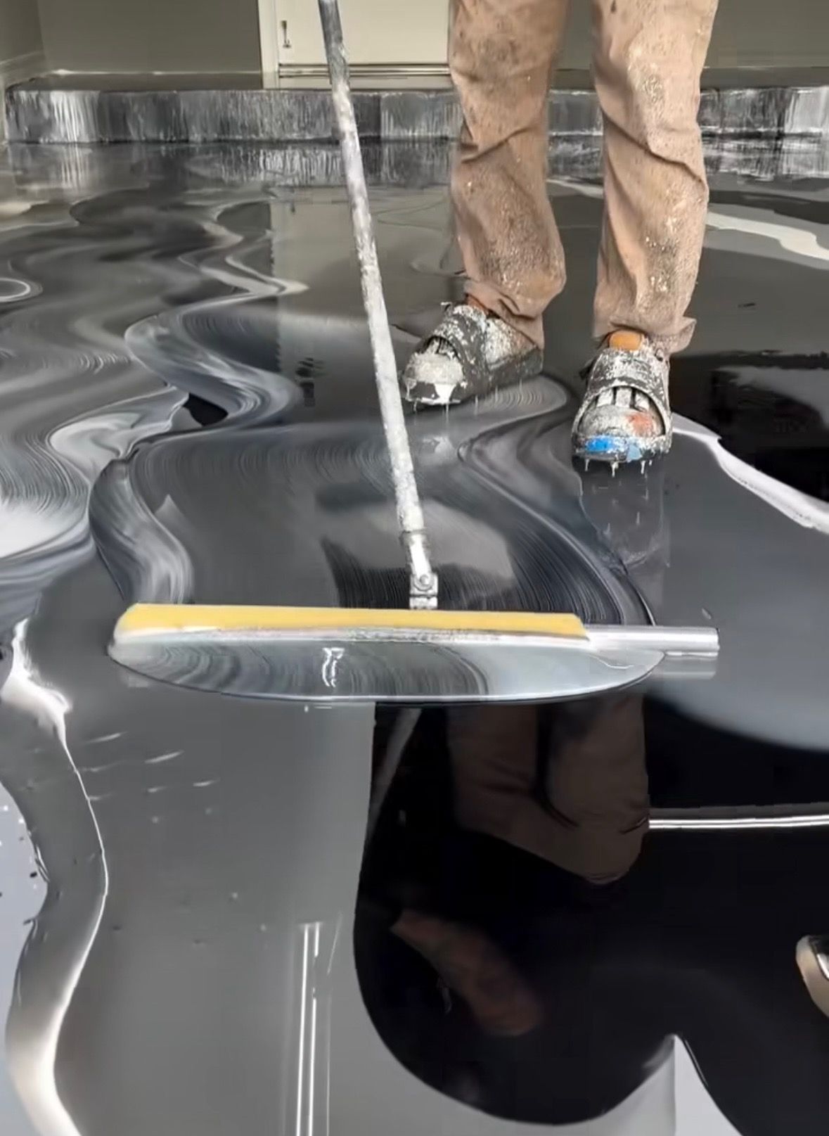 A person is painting a black floor with a broom.