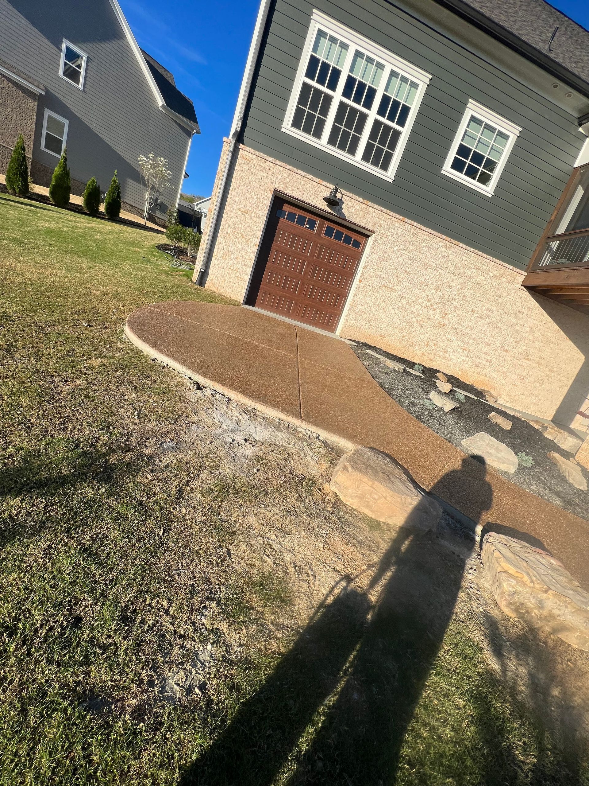A shadow of a person is cast on the grass in front of a house.