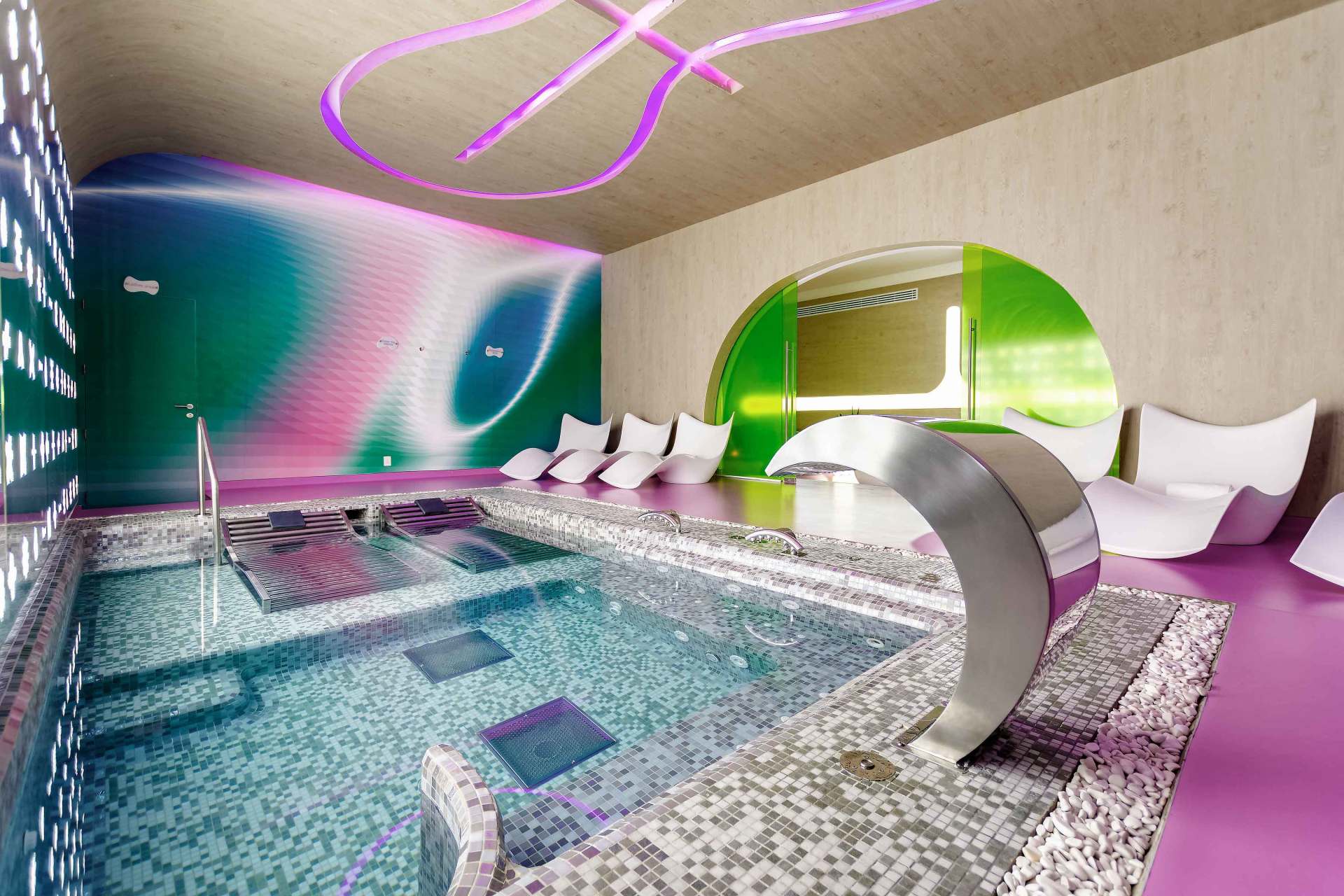 Interior de spa con piscina, luces de neón, paredes curvas y tumbonas.