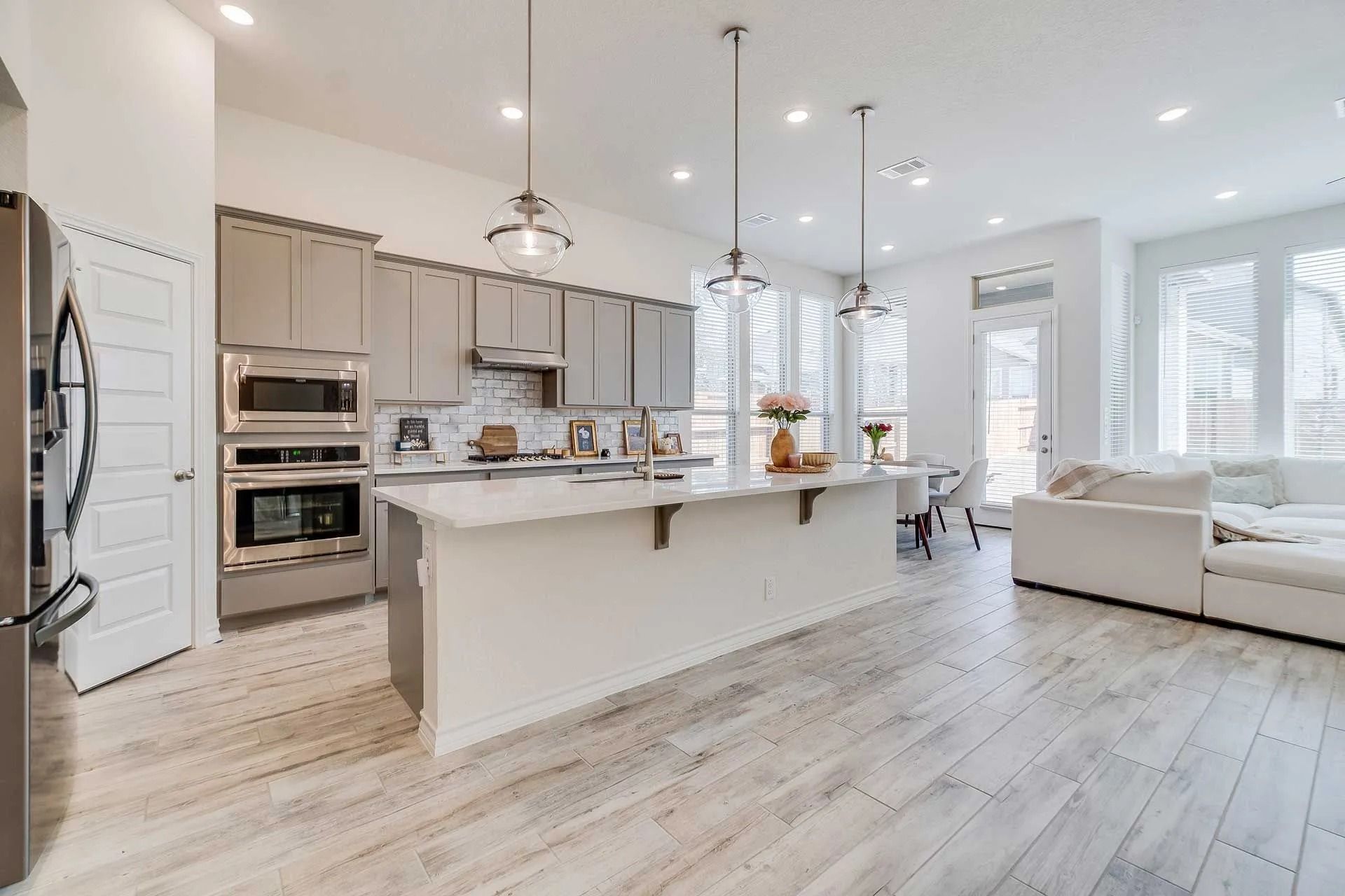 Modern kitchen with island, gray cabinets, stainless steel appliances, and wood-look flooring.