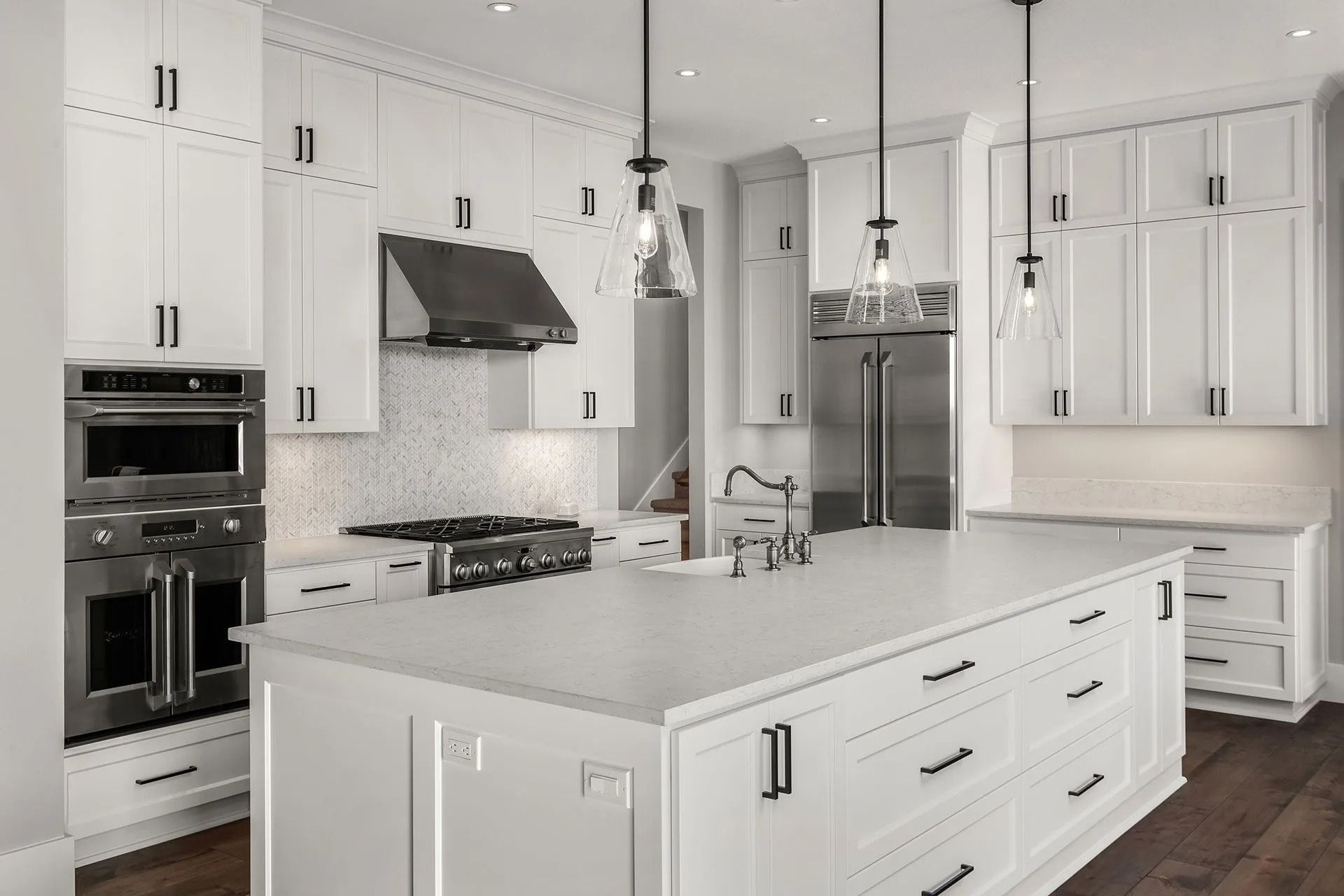 White kitchen with island, stainless steel appliances, black hardware, and pendant lights.