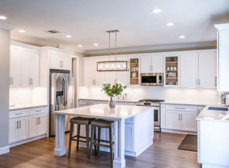 White kitchen with island, stainless steel appliances, and wooden flooring.