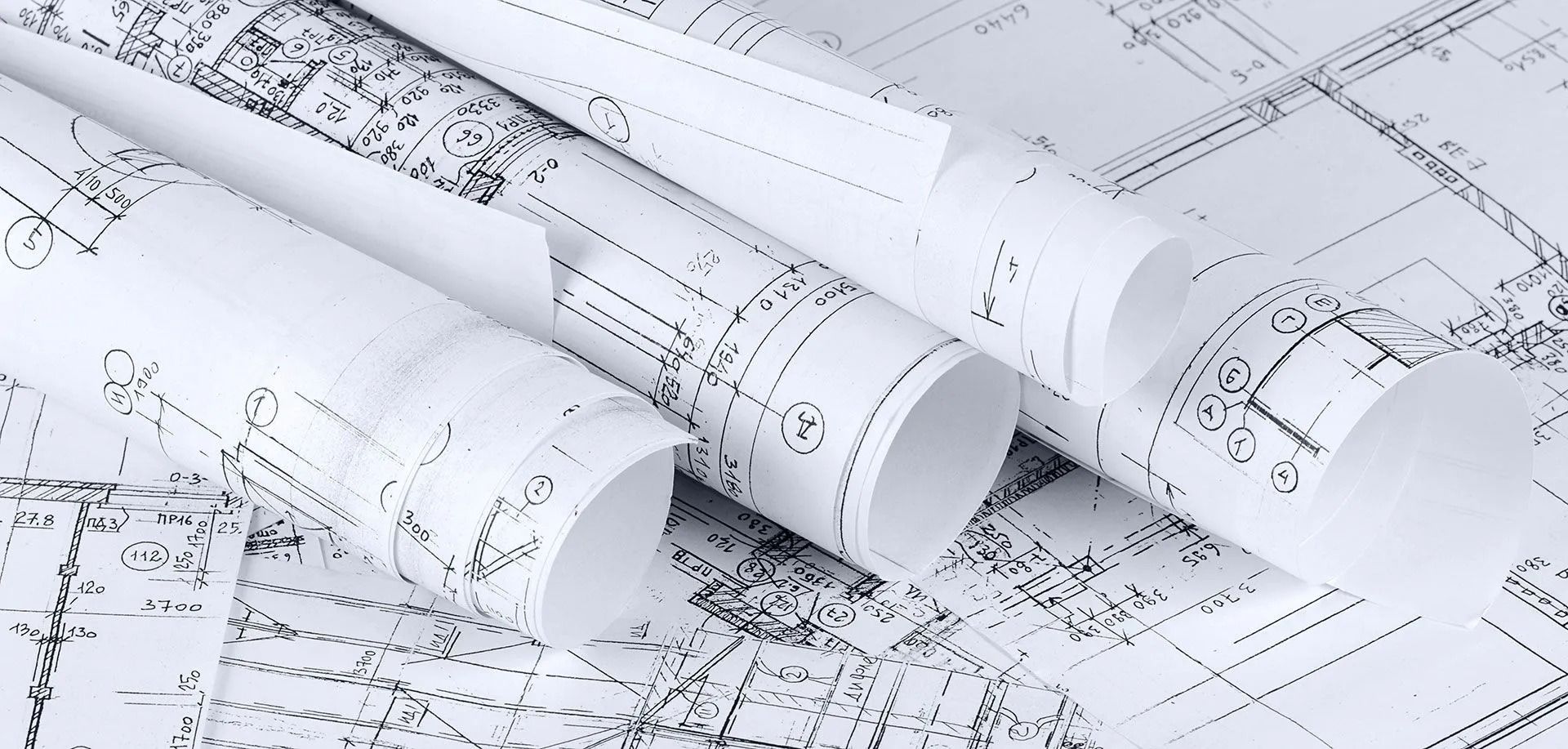 Rolled architectural blueprints spread across a table with technical drawings visible