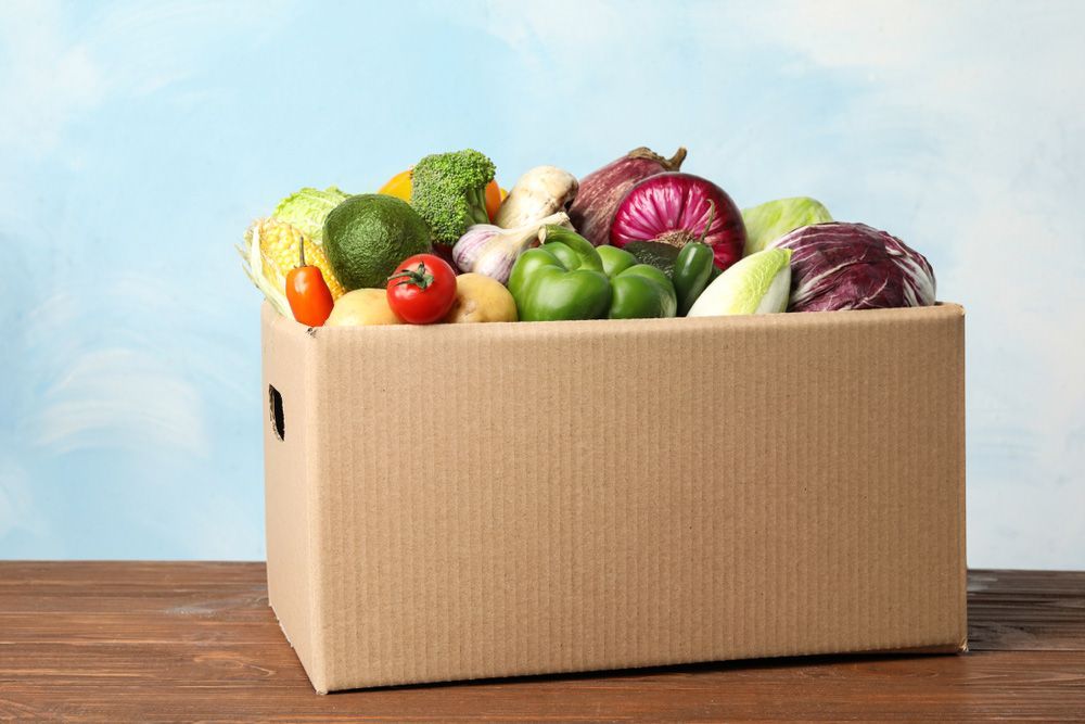 A Cardboard Box Filled With Vegetables On A Wooden Table — Remote Shopping Services In Edge Hill, QLD