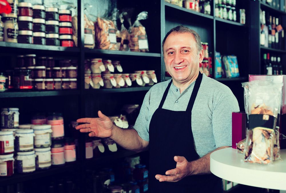 A Man In An Apron Is Standing In Front Of A Table In A Store — Remote Shopping Services In Edge Hill, QLD