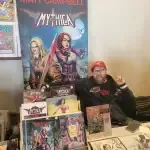 A Man Is Sitting At A Table In Front Of A Poster — Aurora, CO — All C's Collectibles