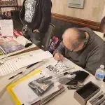 A Man Is Sitting At A Table Writing On A Piece Of Paper — Aurora, CO — All C's Collectibles