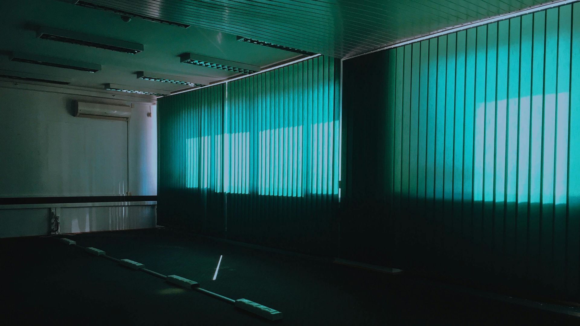 Large teal vertical blinds covering a wall of windows in a modern empty office.
