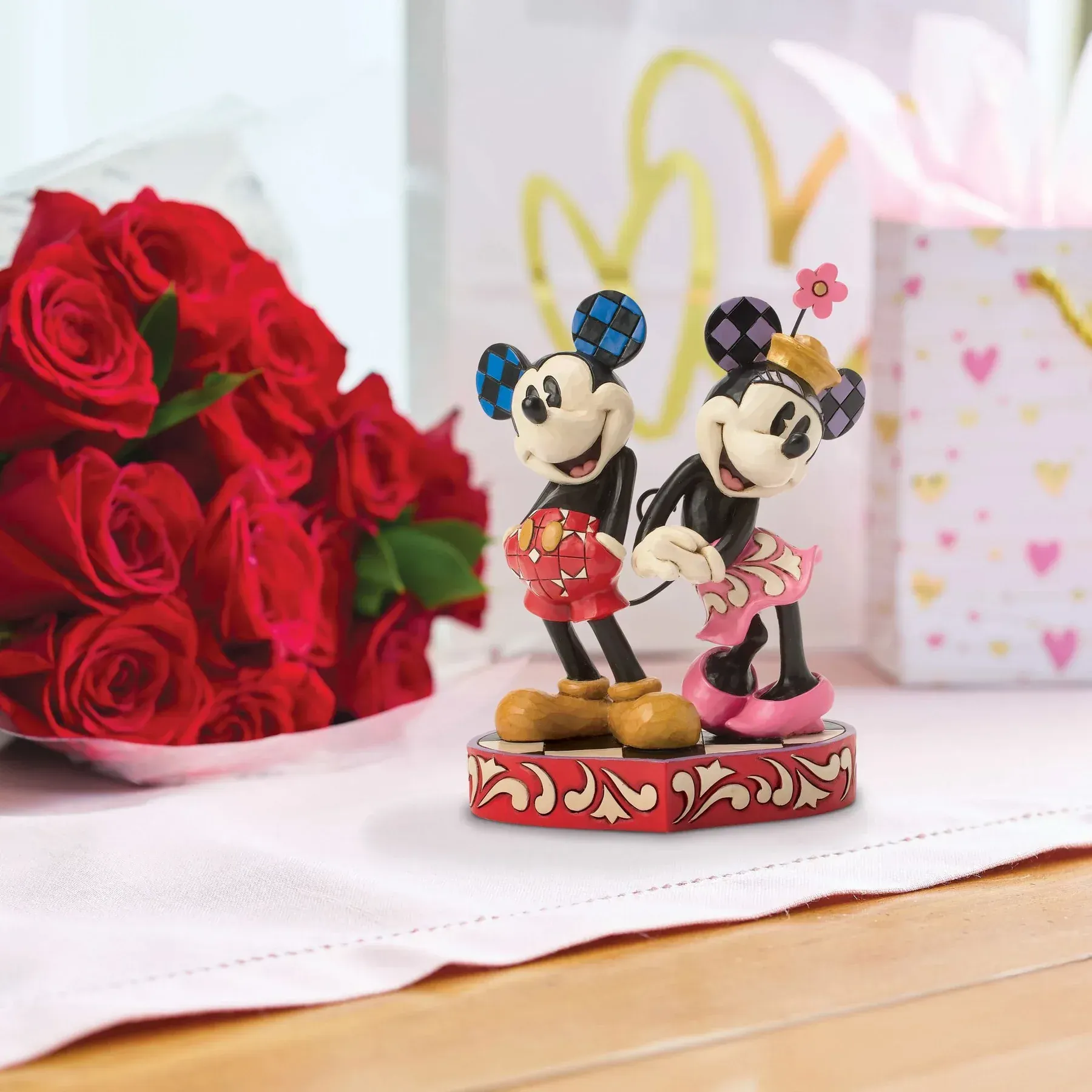 Mickey en Minnie Mouse beeldjes op een decoratieve sokkel, rode rozen en cadeautasjes.