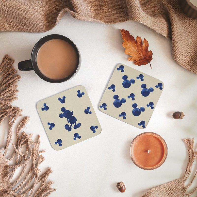 Twee Mickey Mouse-onderzetters staan op een tafel naast een kop koffie en een kaars.