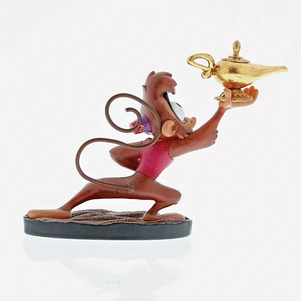 Het beeldje van aapje Abu, die een gouden lamp vasthoudt, zit gehurkt en heeft een verbaasde uitdrukking.