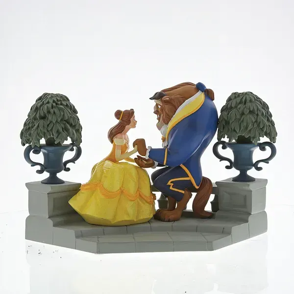 Een beeldje van Belle en het Beest, knielend, geplaatst op stenen trappen, met twee potbomen.