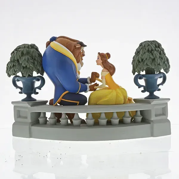 Een beeldje van Belle en het Beest op een balkon, het Beest op één knie, Belle zittend, beiden kijkend naar elkaar.