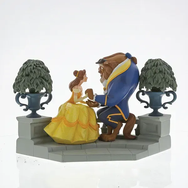 Een beeldje van Belle en het Beest, knielend, geplaatst op stenen trappen, met twee potbomen.