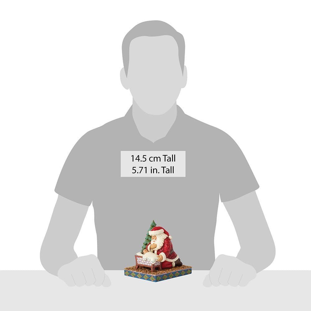 Een beeldje van de Kerstman die knielt en een baby in een wiegje vasthoudt.