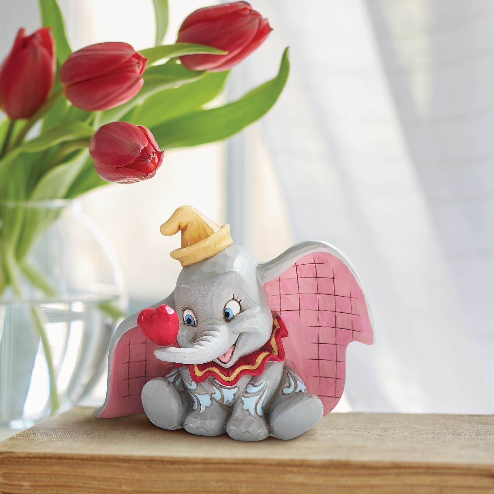 Een beeldje van dumbo zit op een tafel voor een vaas met rode tulpen