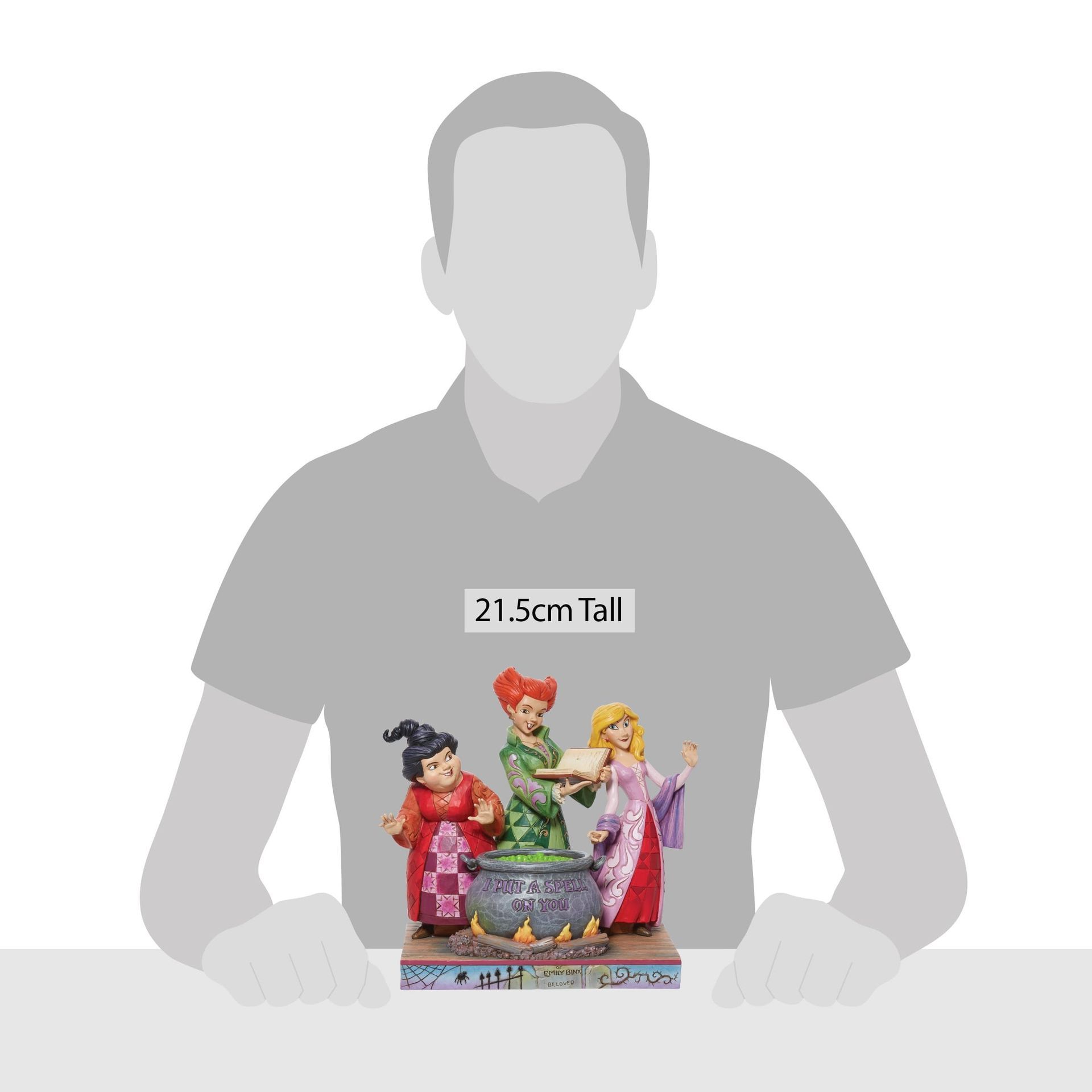 Een man zit aan een tafel met een beeldje van drie heksen.