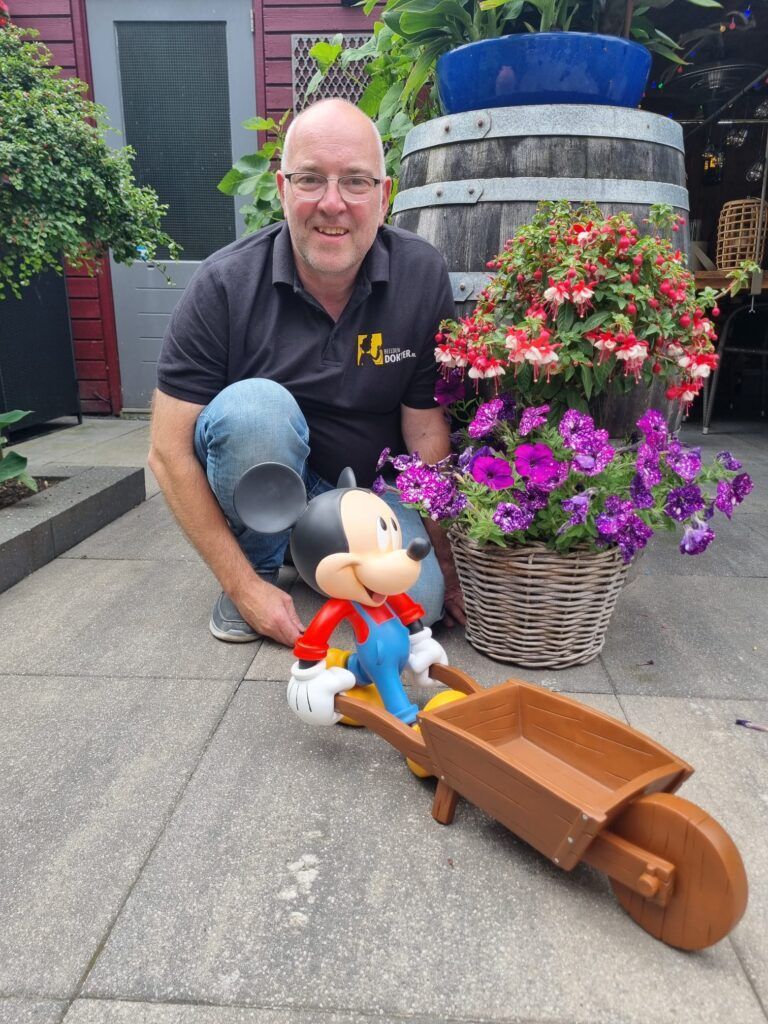 Een man knielt naast een Mickey Mouse-beeldje en een kruiwagen.