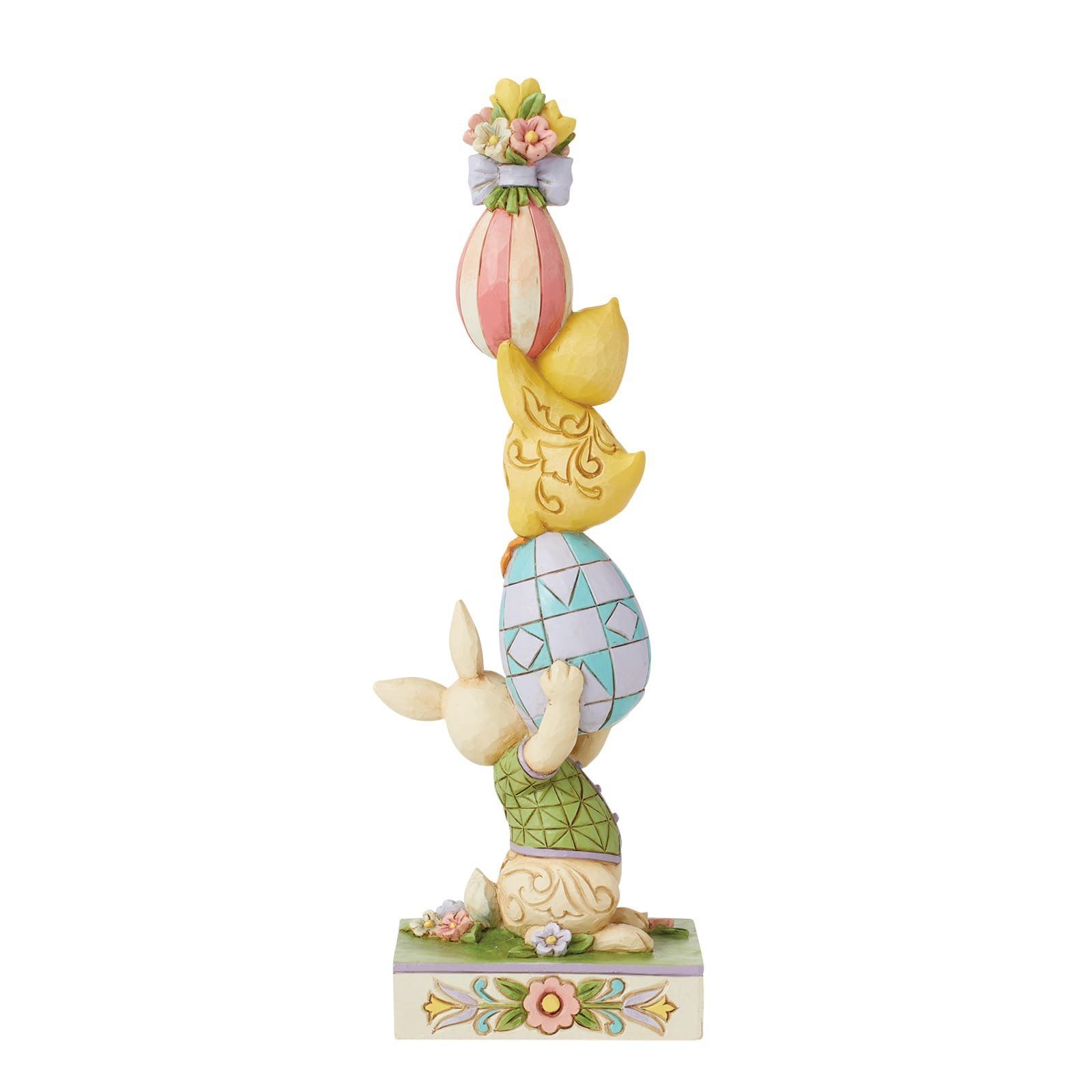 Een beeldje van een konijn dat bovenop een stapel paaseieren staat.