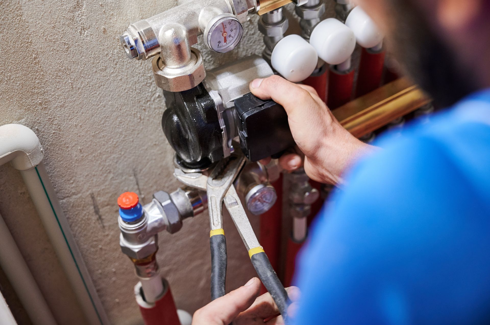 Plumber using pliers on a heating system pump, near pipes and gauges.